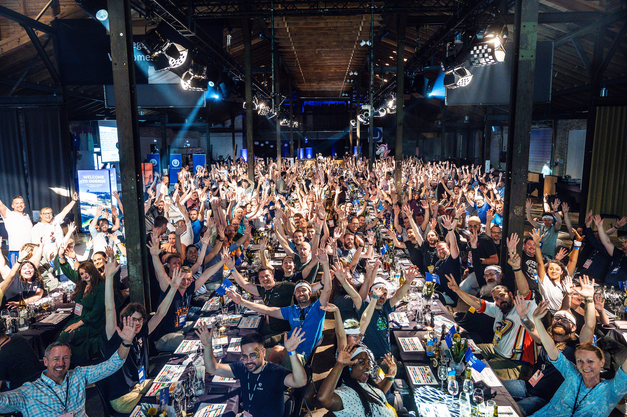 Codegarden 2023 attendees sat at long tables, with hands raised in the air ready to play bingo!