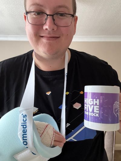 Liam Goldfinch wearing an Umbraco shirt, holding a High Five You Rock mug, while using an arm sling.