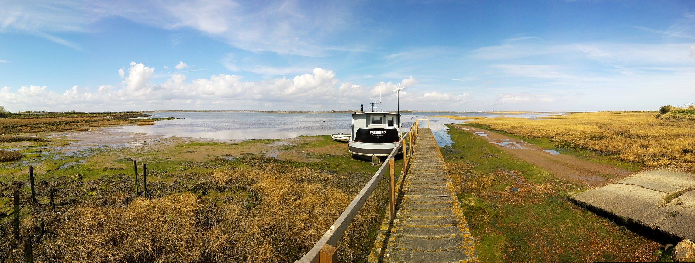 A boat moored at the end of a gangway with the tide out. The boat is named Freebird.